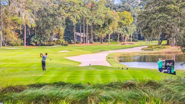 A golf course with a water hazard, sand bunkers, and a clubhouse in the background. - 148 Island House @ Forest Beach | Walk to Beach | Pool | Pet-Friendly | Tennis (Hilton Head Island)