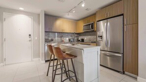 A modern kitchen with stainless steel appliances, wooden cabinets, and a central island with bar stools. - Prime Downtown Doral Park Condo (Doral)
