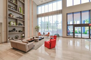 Un vestíbulo amplio con un sofá color beige, sillas rojas y una estantería llena de objetos decorativos.