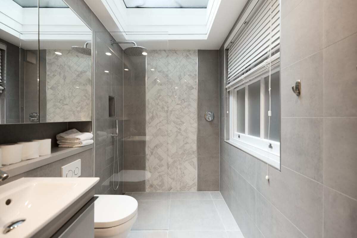 Et moderne badeværelse med ovenlys, brusekabine i glas og toilet.
