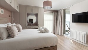 A modern bedroom with a large bed, a built-in wardrobe, a mirror, a flat-screen TV, and a view of the outdoors. - 3 St Nicholas Court - St Ives (St Ives)