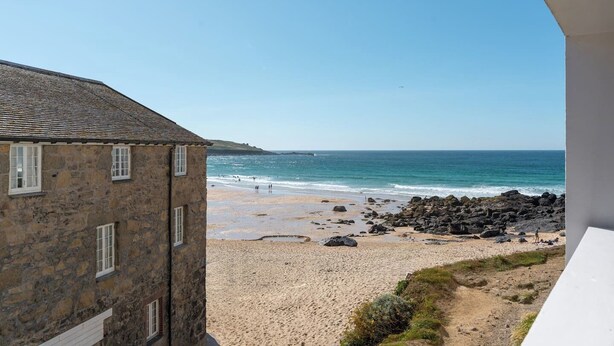 A stone building with a sloped roof overlooking a beach with rocky areas and a clear view of the ocean. - 3 St Nicholas Court - St Ives (St Ives)