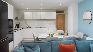 A modern kitchen with white cabinets, a marble backsplash, and a dining area with a table set for breakfast. - 3 St Nicholas Court - St Ives (St Ives)