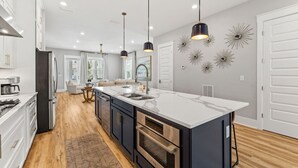 Une cuisine moderne dotée d’un grand îlot central, d’appareils électroménagers en acier inoxydable et de luminaires suspendus.