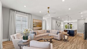 Un salon moderne avec un canapé d’angle beige, une table basse et un coin repas, la cuisine étant visible à l’arrière-plan.