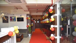 A reception area with a red carpet, a reception desk, and a wall decorated with balloons. - Hotel Crown Castle (Guwahati)