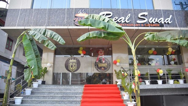 A building with a sign reading "Real Swad Restaurant & Caterer" and a logo above the entrance. - Hotel Crown Castle (Guwahati)