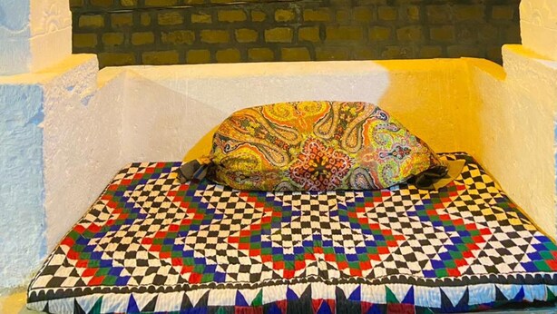 A bed with a colorful patterned blanket and pillow, set in a room with a view of a cityscape at night. - Muki Guest House By GRB (Jaisalmer)