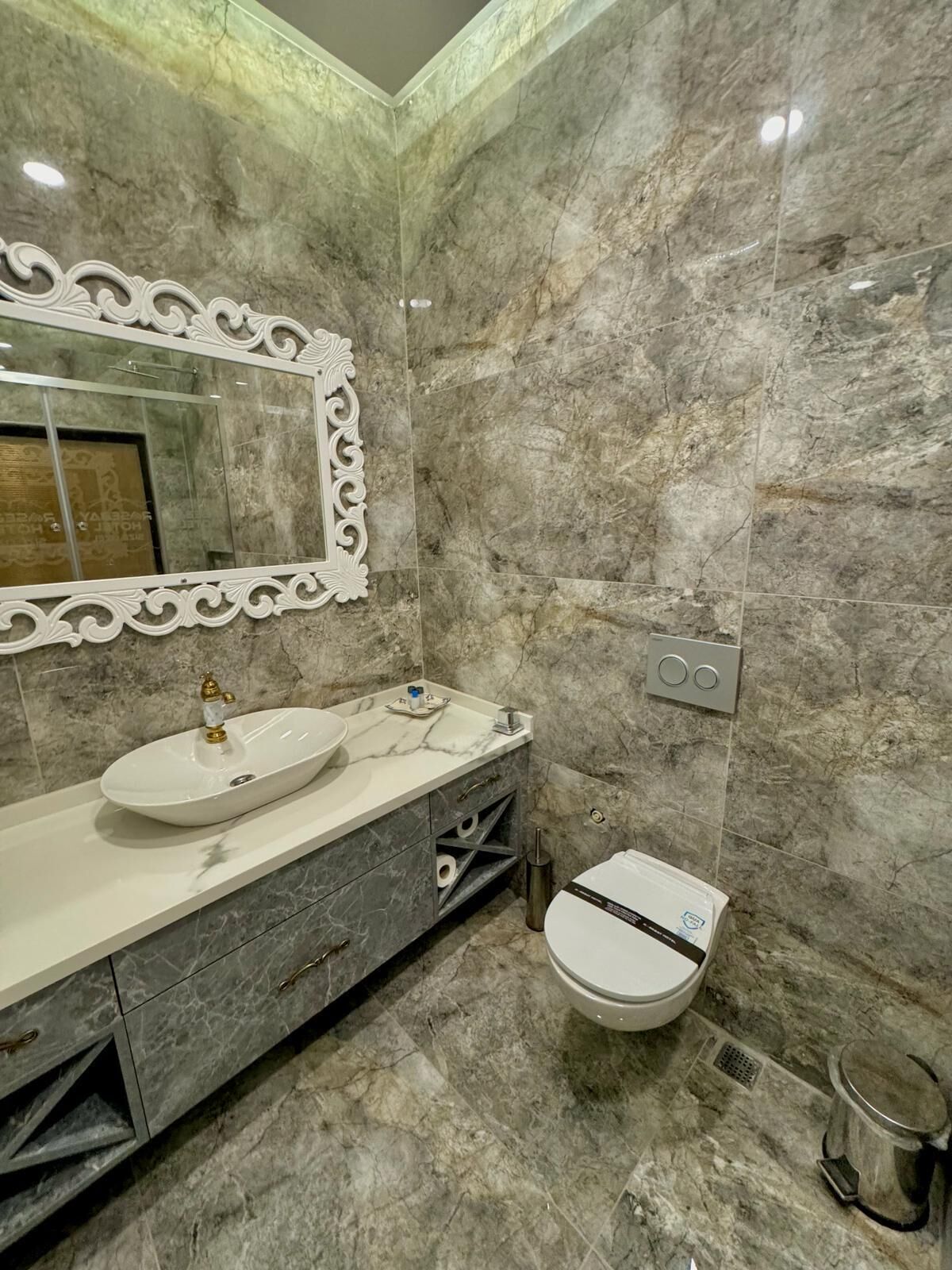 A bathroom with a marble sink, vanity, and toilet.