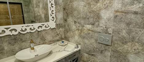 Un baño con lavamanos, tocador e inodoro de mármol.