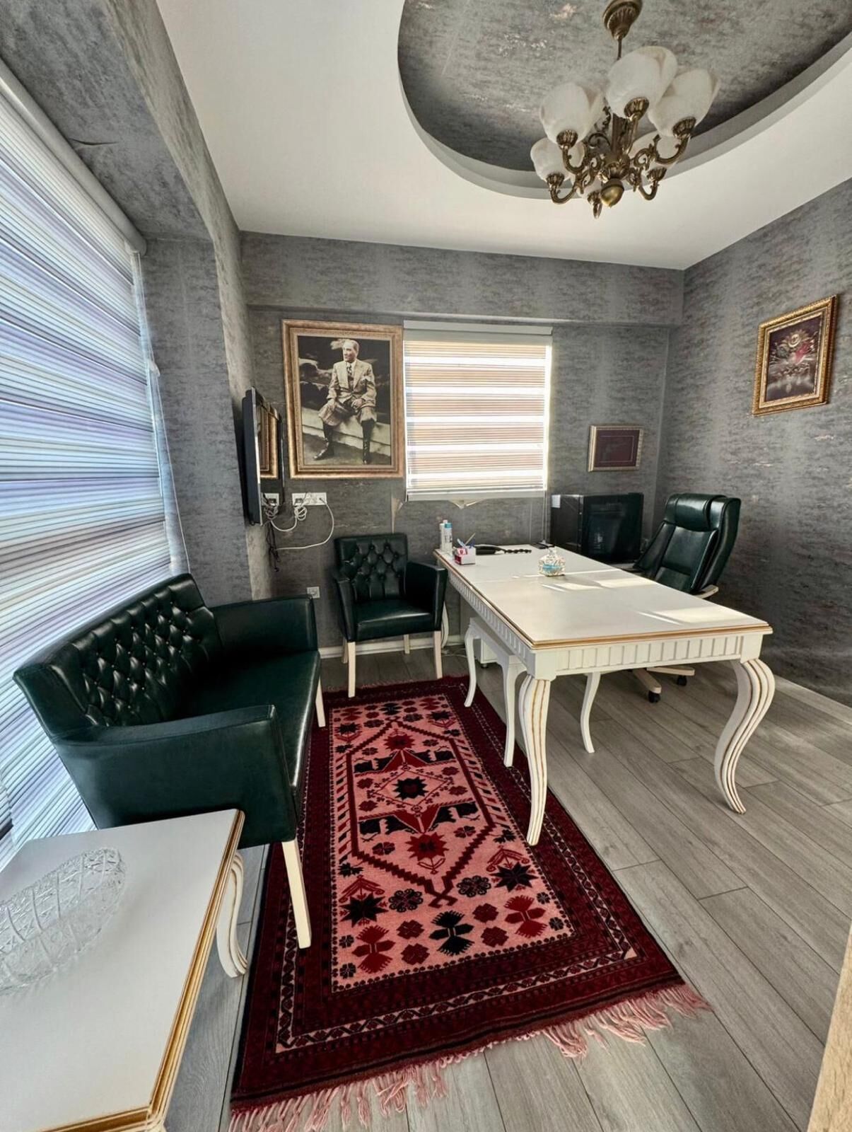 A dining room with a white table, two black chairs, a red patterned rug, and a chandelier.