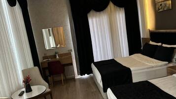 Habitación de hotel con dos camas, un escritorio, una silla y una mesita con un florero.