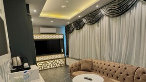 A modern living room with a sectional sofa, a round coffee table, and a flat-screen TV. - Golden Rose Deluxe Hotel (Manisa)