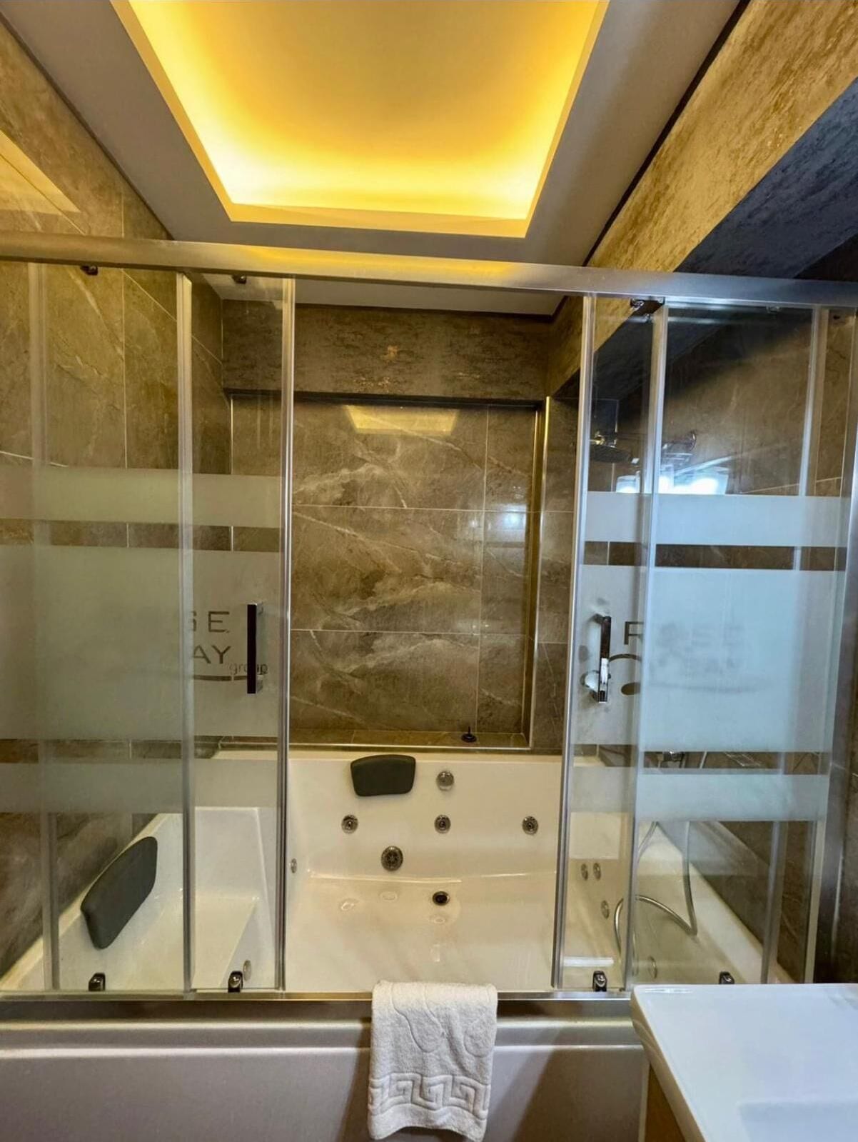 A modern bathroom with a glass-enclosed shower, marble tiles, and a white bathtub.