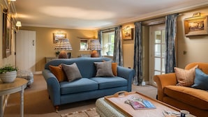 A living room with a blue sofa, an orange sofa, a coffee table with magazines, and a side table with a plant. - Otmoor House - Beckley, Near Oxford (Beckley)