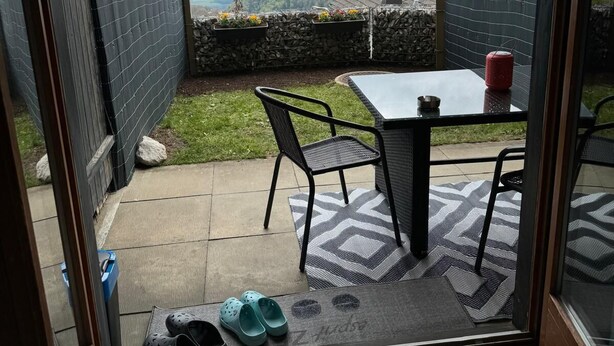 Une terrasse avec une table et des chaises, une paire de crocs et une tasse rouge.