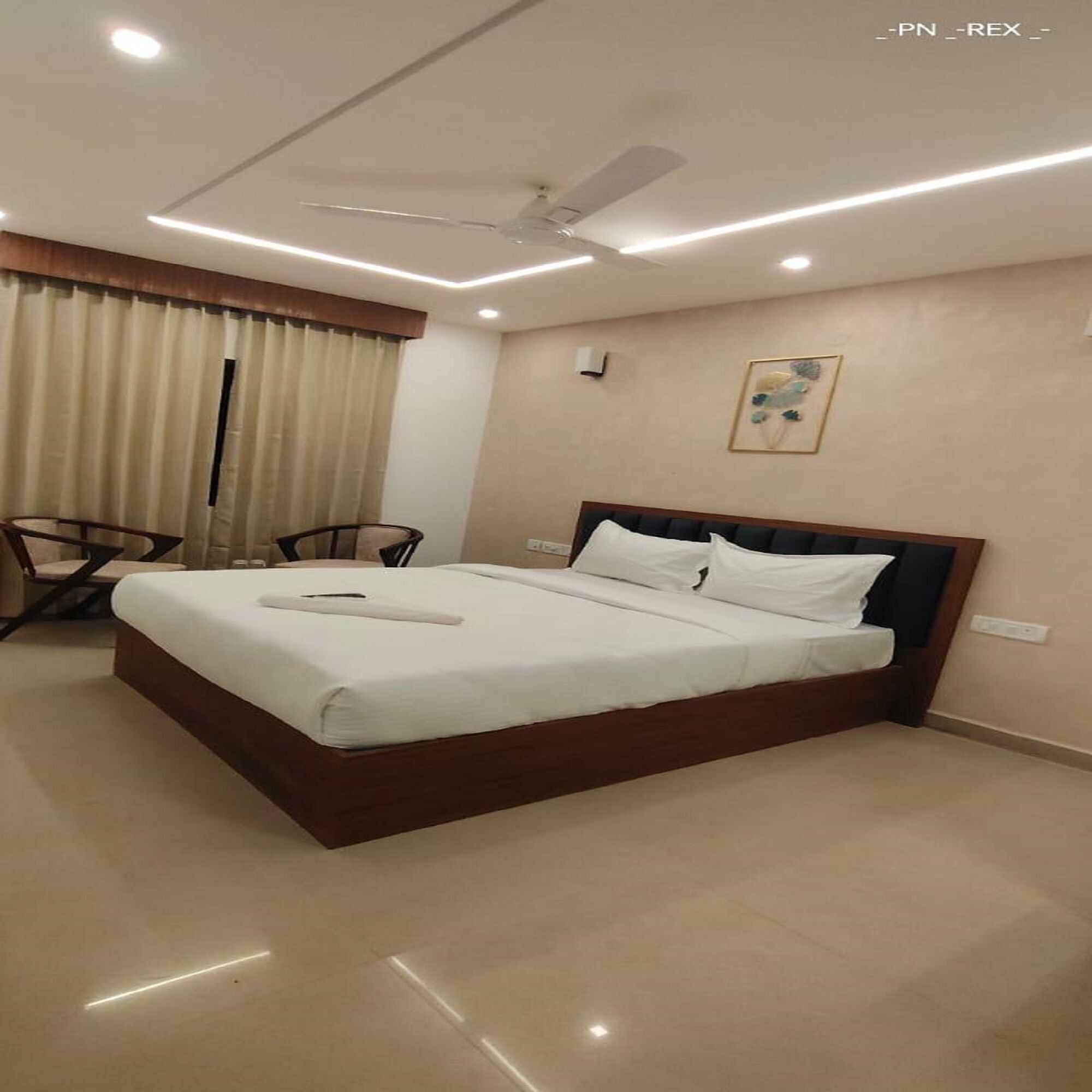 A hotel room with a bed, a ceiling fan, a chair, and a wall-mounted light.