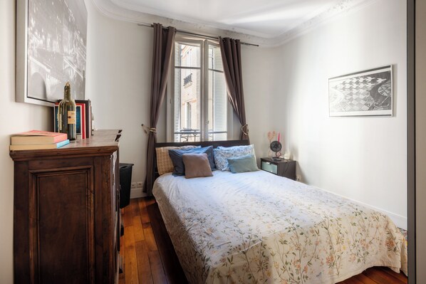 A bedroom with a bed, a nightstand, a dresser, a window with curtains, and a wall-mounted picture.