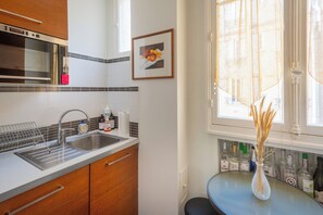 A kitchen with a stainless steel sink, wooden cabinets, a microwave, and a window with a view of the city.