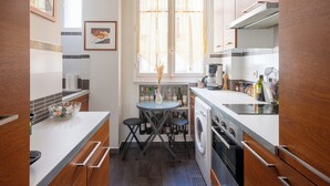 A compact kitchen with a dining area, a washing machine, and a window with curtains. - Opulent 1BD Apartment near Eiffel Tower, Grenelle (Paris)