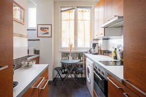 A compact kitchen with a washing machine, a dining table, and a window with curtains.