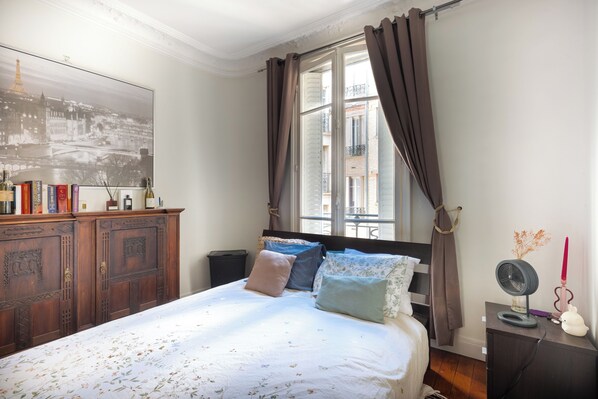 A bedroom with a bed, a dresser, a window with curtains, and a wall-mounted picture.