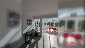 A modern interior with a staircase leading to a conservatory, a dining area with red chairs, and a view of greenery outside. - Thames Riverside Retreat: A Serene 3-Bed Bungalow (Surrey)