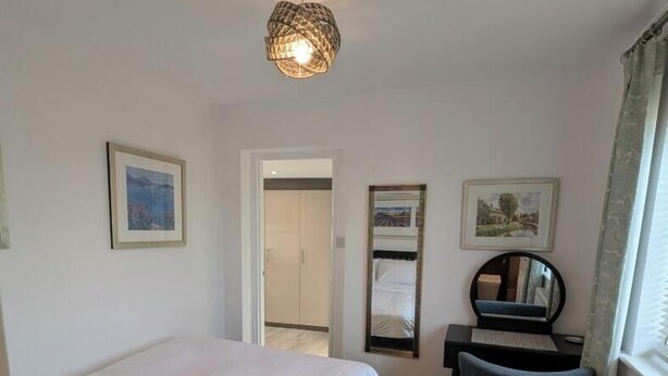 A bedroom with a bed, a desk, a chair, a mirror, and a hanging light fixture. - Thames Riverside Retreat: A Serene 3-Bed Bungalow (Surrey)