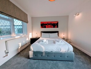 A bedroom with a large bed, two bedside tables, a radiator, and a window with blinds.