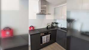 A modern kitchen with black countertops, stainless steel appliances, and a red first aid bag. - Thames Riverside Retreat: A Serene 3-Bed Bungalow (Surrey)