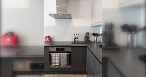 A modern kitchen with a built-in oven, a stainless steel range hood, and a countertop with kitchen utensils. - Thames Riverside Retreat: A Serene 3-Bed Bungalow (Surrey)