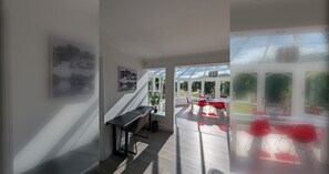 A modern interior with a staircase leading to a conservatory, a dining area with red chairs, and a view of greenery outside. - Thames Riverside Retreat: A Serene 3-Bed Bungalow (Surrey)