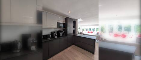 A modern kitchen with dark cabinetry, a wooden countertop, and a view of an outdoor seating area.