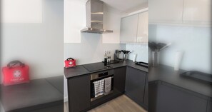 A modern kitchen with black countertops, stainless steel appliances, and a red first aid bag. - Thames Riverside Retreat: A Serene 3-Bed Bungalow (Surrey)