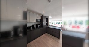 A modern kitchen with dark cabinetry, a wooden countertop, and a view of an outdoor seating area. - Thames Riverside Retreat: A Serene 3-Bed Bungalow (Surrey)