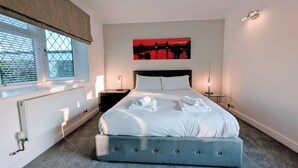 A bedroom with a large bed, two bedside tables, a radiator, and a window with blinds.