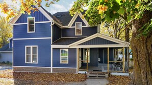 A two-story house with a covered porch and a large tree in front. - Walk to Platt River, Game Room, Hot Tub,Indoor Pickleball, Kayaks, Bikes, Arcade (Honor)
