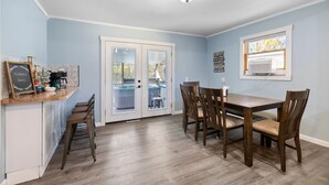 A dining area with a wooden table and chairs, a kitchen counter with bar stools, and a sliding glass door leading to an outdoor patio. - Walk to Platt River, Game Room, Hot Tub,Indoor Pickleball, Kayaks, Bikes, Arcade (Honor)