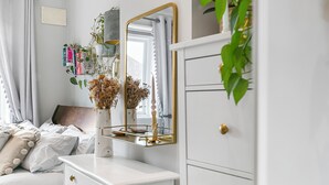 A bedroom with a white dresser, a mirror, and a bedside table. There is a plant on the dresser and a window with curtains. - Charming 2BR Family Home with Private Garden (Greater London)