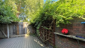 Una terraza de madera con un muro de ladrillo y una valla metálica.
