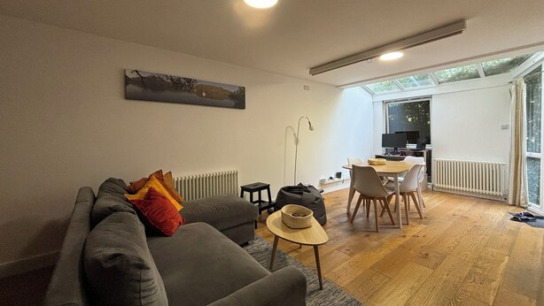 Una sala de estar moderna con un sofá gris, una mesa de comedor con sillas, un radiador y un ventanal grande.