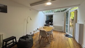 Un espacio habitable pequeño con comedor, un sillón de peluche, una lámpara de pie y vistas al exterior a través de una puerta corrediza de vidrio.