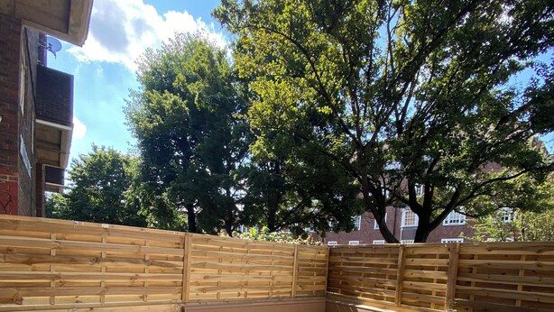 Een houten terras met een ingebouwde zithoek, een bakstenen muur en een potplant.