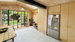 Una cocina con un ventanal grande, una mesa de comedor y un frutero, y un refrigerador con notas e imanes.