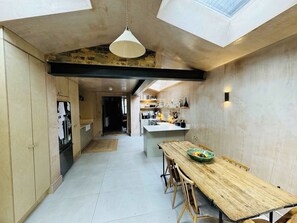 Une cuisine moderne dotée d’un îlot central, d’un coin repas avec une table en bois et d’une lucarne au-dessus.