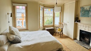 Un dormitorio con una cama grande, una silla, una chimenea y varias ventanas.