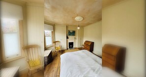 Een slaapkamer met een bed, een houten dressoir, een stoel, een open haard en een raam.