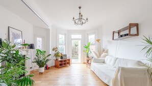 Una habitación luminosa y amplia con sofá blanco, suelo de madera y ventanas grandes.