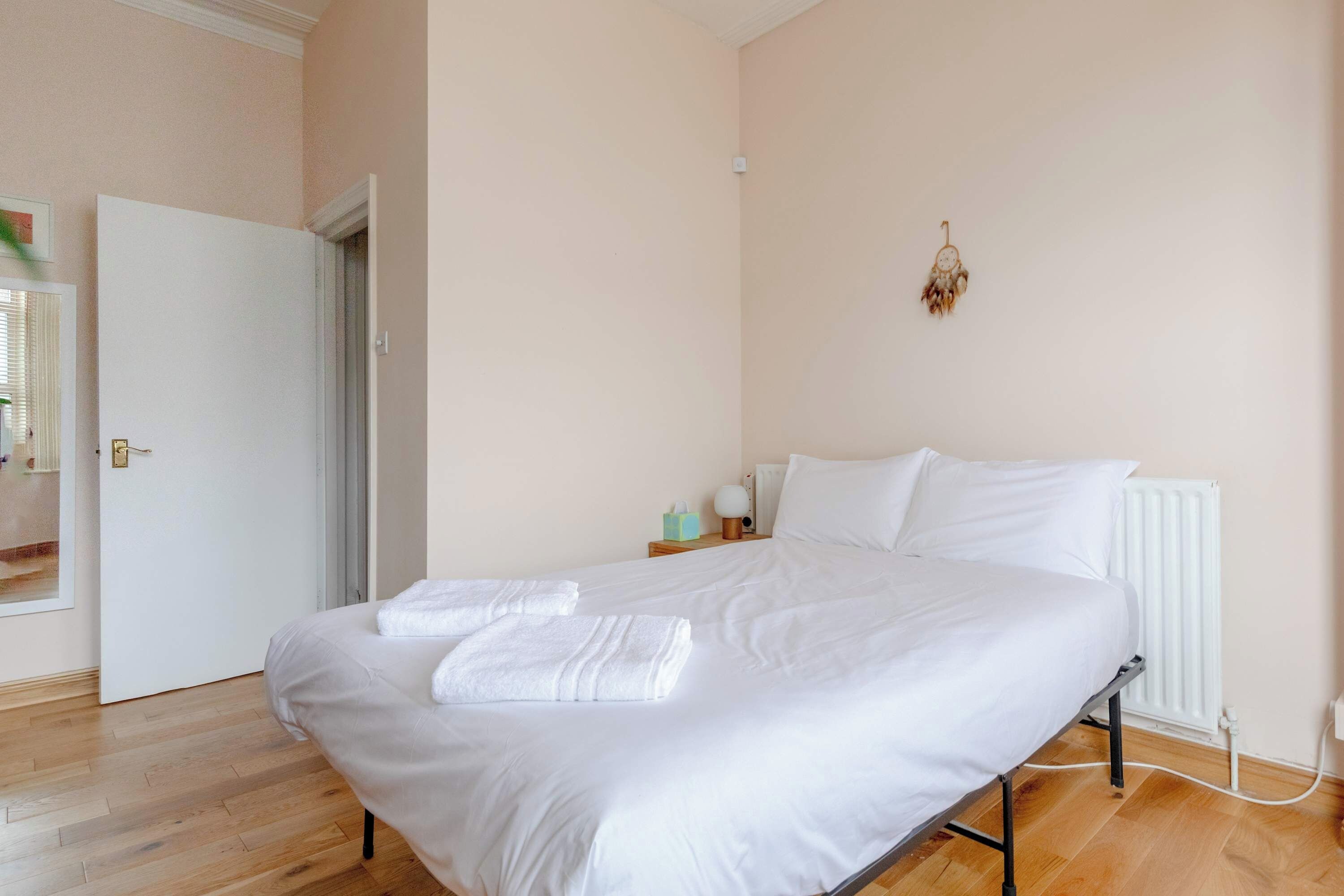 A bedroom with a bed, a bedside table, a nightstand, a wall clock, and a radiator.