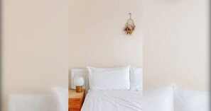 Quarto minimalista com cama, mesa de cabeceira e um sonhoapanha pendurado na parede.